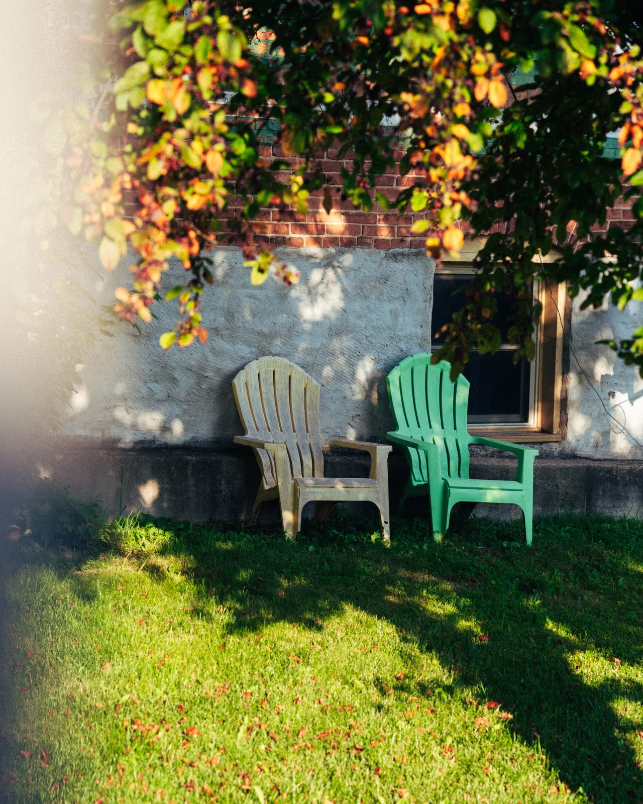 Two Adirondack chairs under leafy branches beside a brick house in Berlin, Wisconsin
