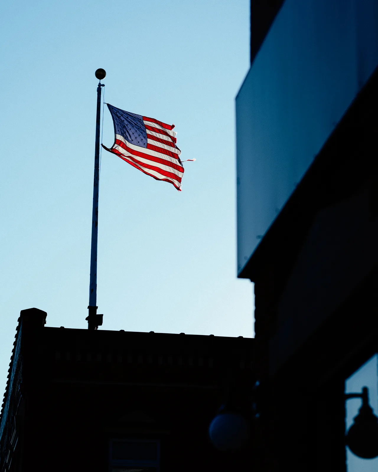 A worn American flag flying between shadowed downtown buildings