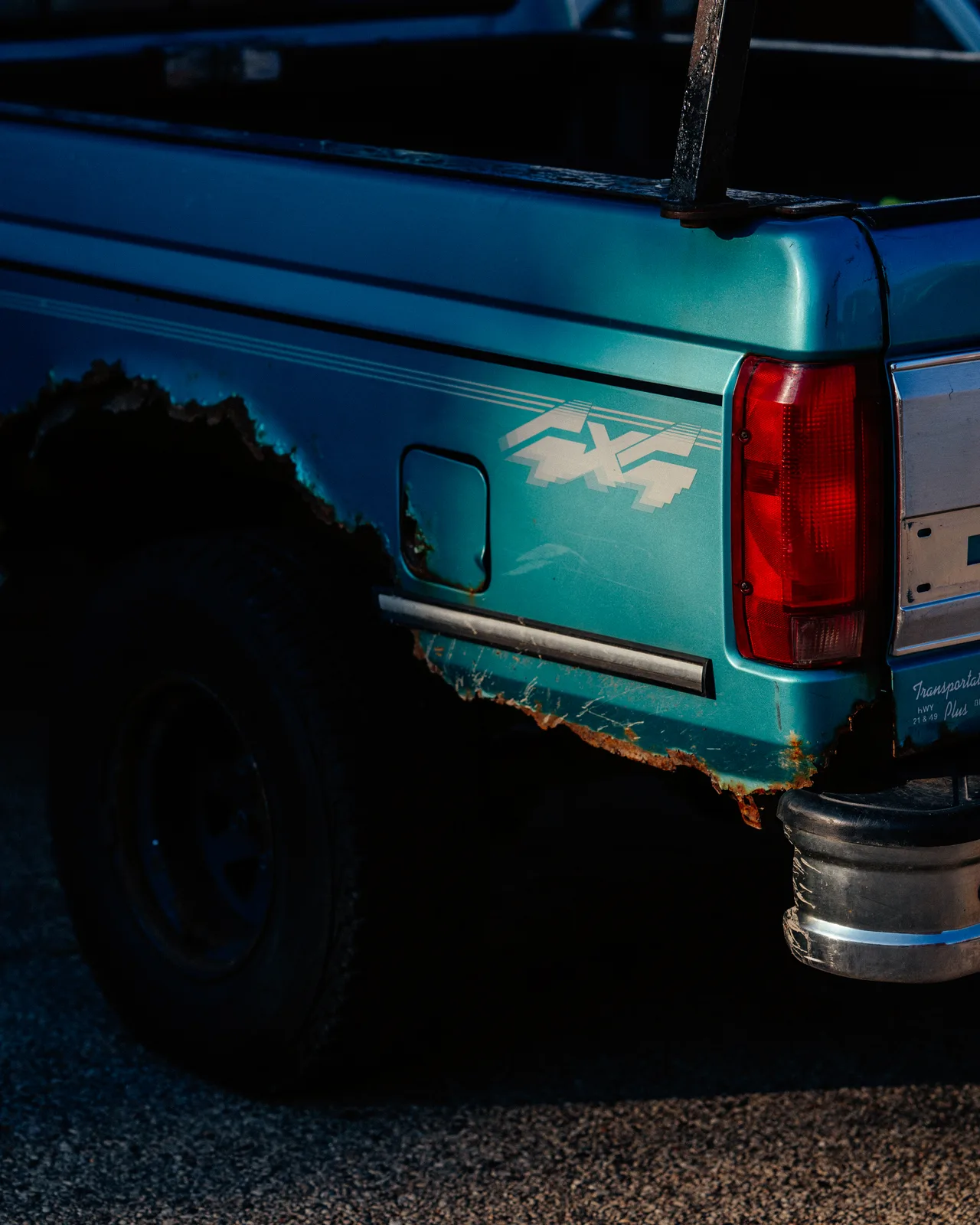 The sunlit rear corner of a turquoise four-wheel-drive pickup