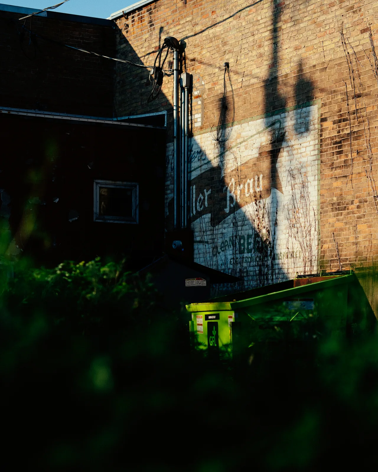 A faded painted wall sign and green dumpster behind a brick building