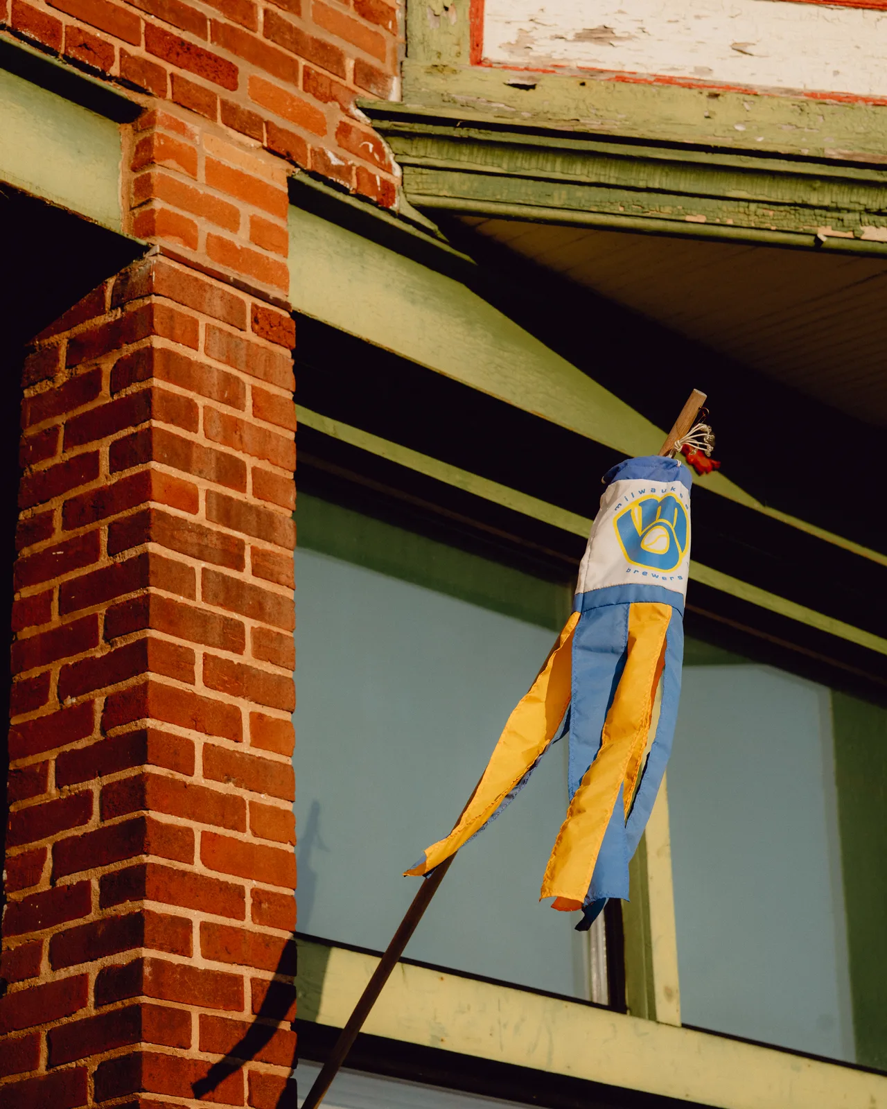 A Milwaukee Brewers windsock against brick and peeling green trim