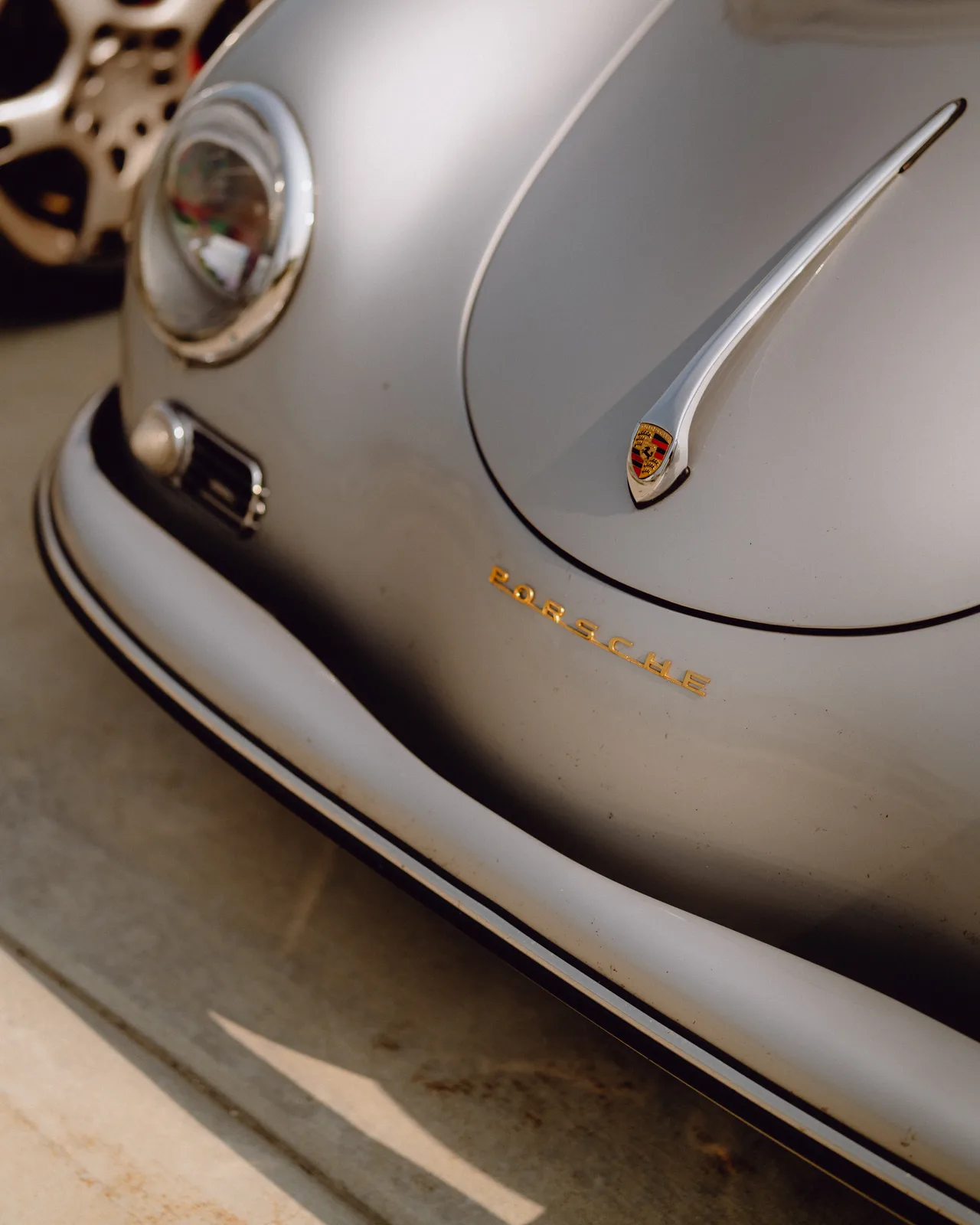 Close view of the rounded hood and headlamp of Curt Cromwell’s silver Porsche Speedster