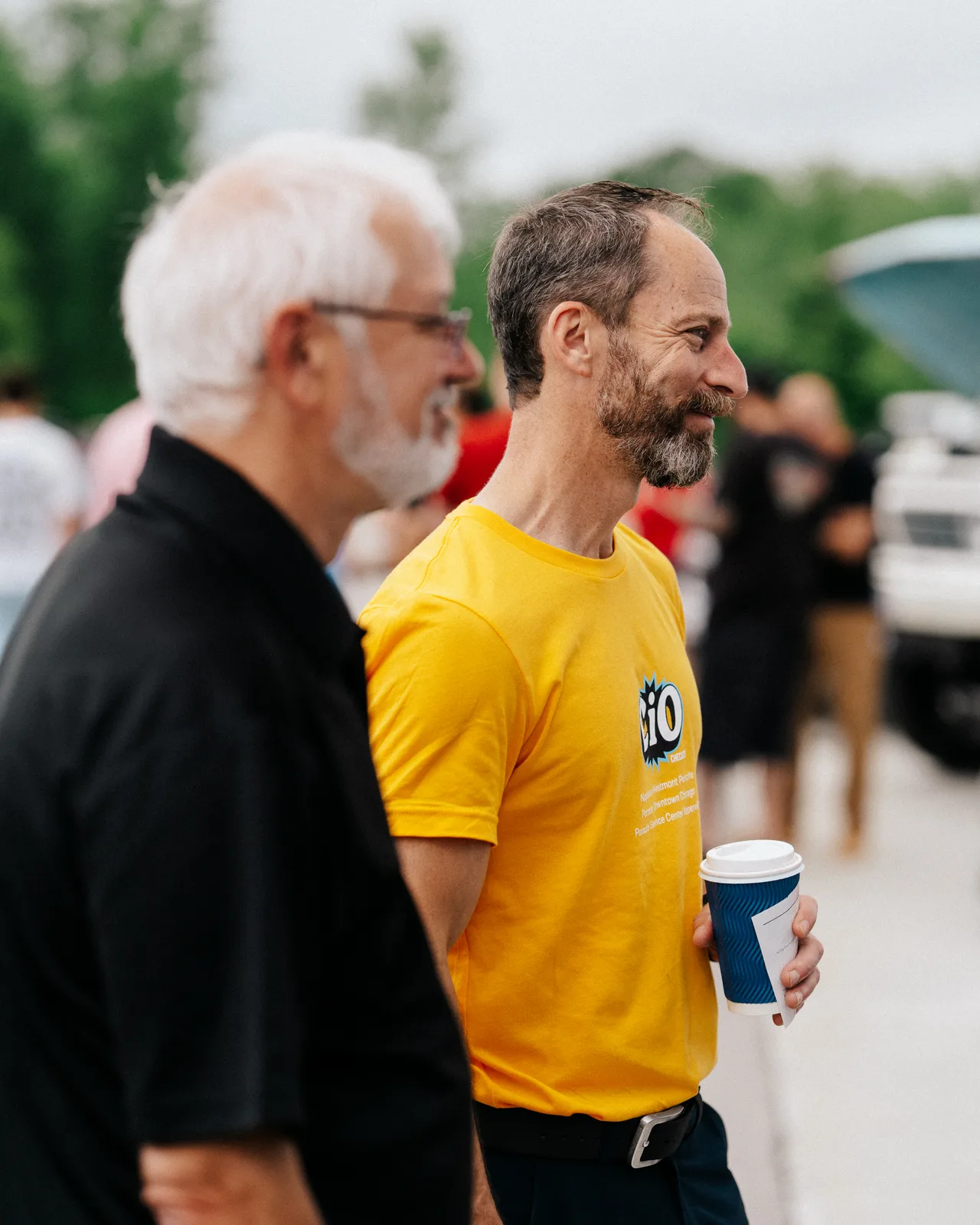 A Checkeditout crew member in a yellow shirt talking with guests at Cars and Coffee